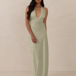 Woman wearing a true sage halter neck dress in jacquard fabric standing  against a beige background