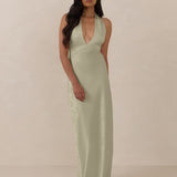 Woman wearing a true sage halter neck dress in jacquard fabric standing  against a beige background