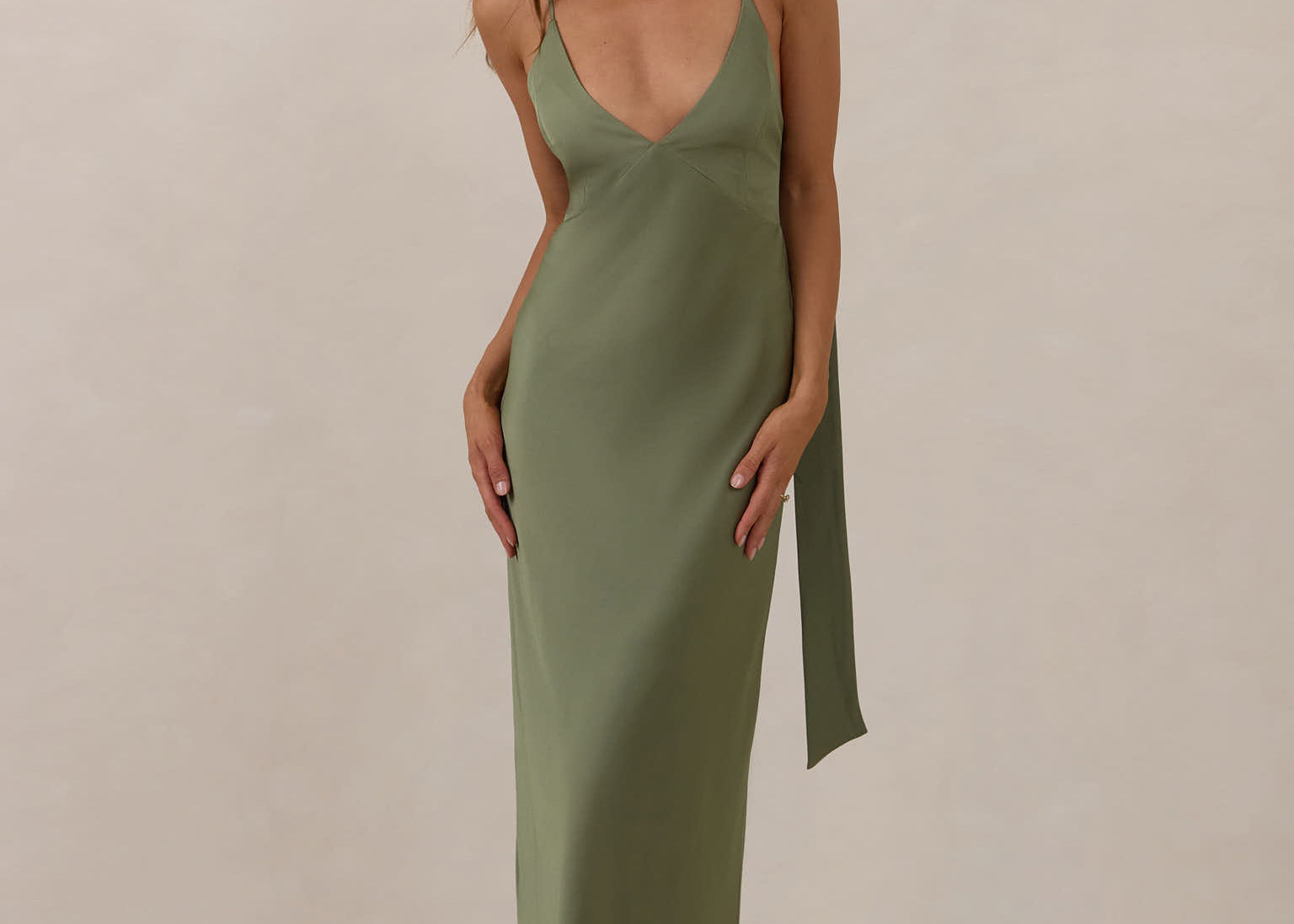 Woman wearing a olive coloured, deep V neck dress against a plain background