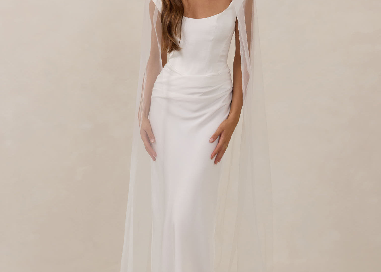 Woman wearing a white wedding dress with a sheer veil against a plain background