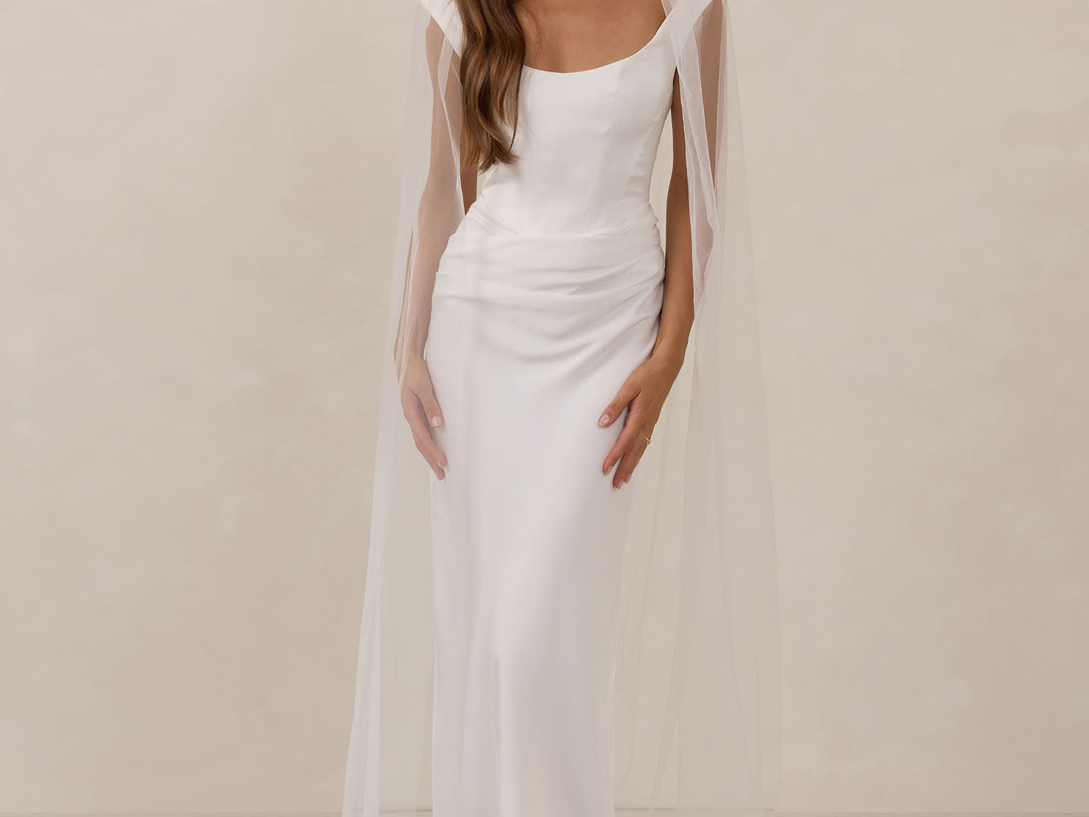 Woman wearing a white wedding dress with a sheer veil against a plain background