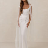 Woman wearing a white wedding dress with a sheer veil against a plain background