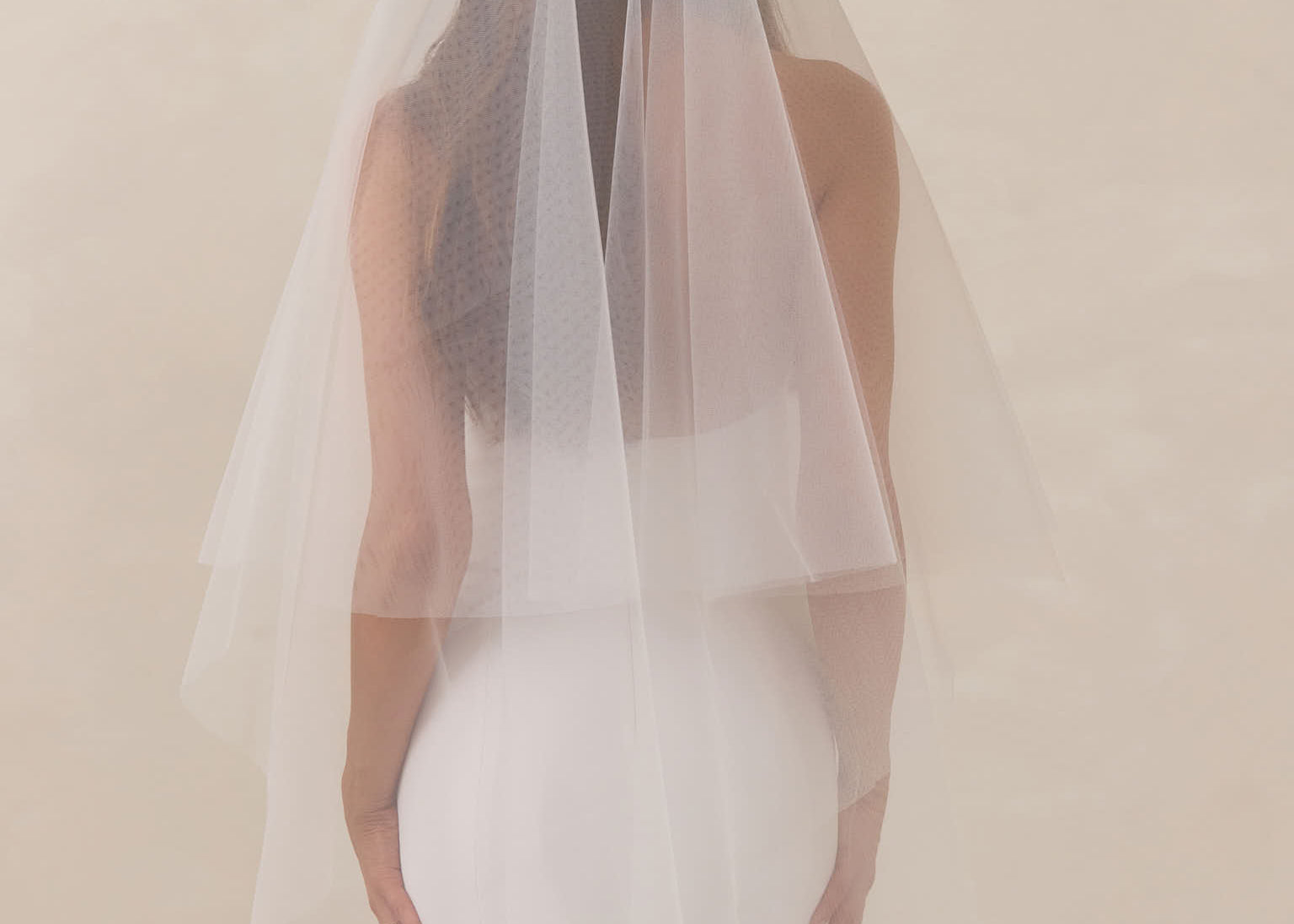 Bride wearing a white wedding dress with a fingertip length veil against a plain background