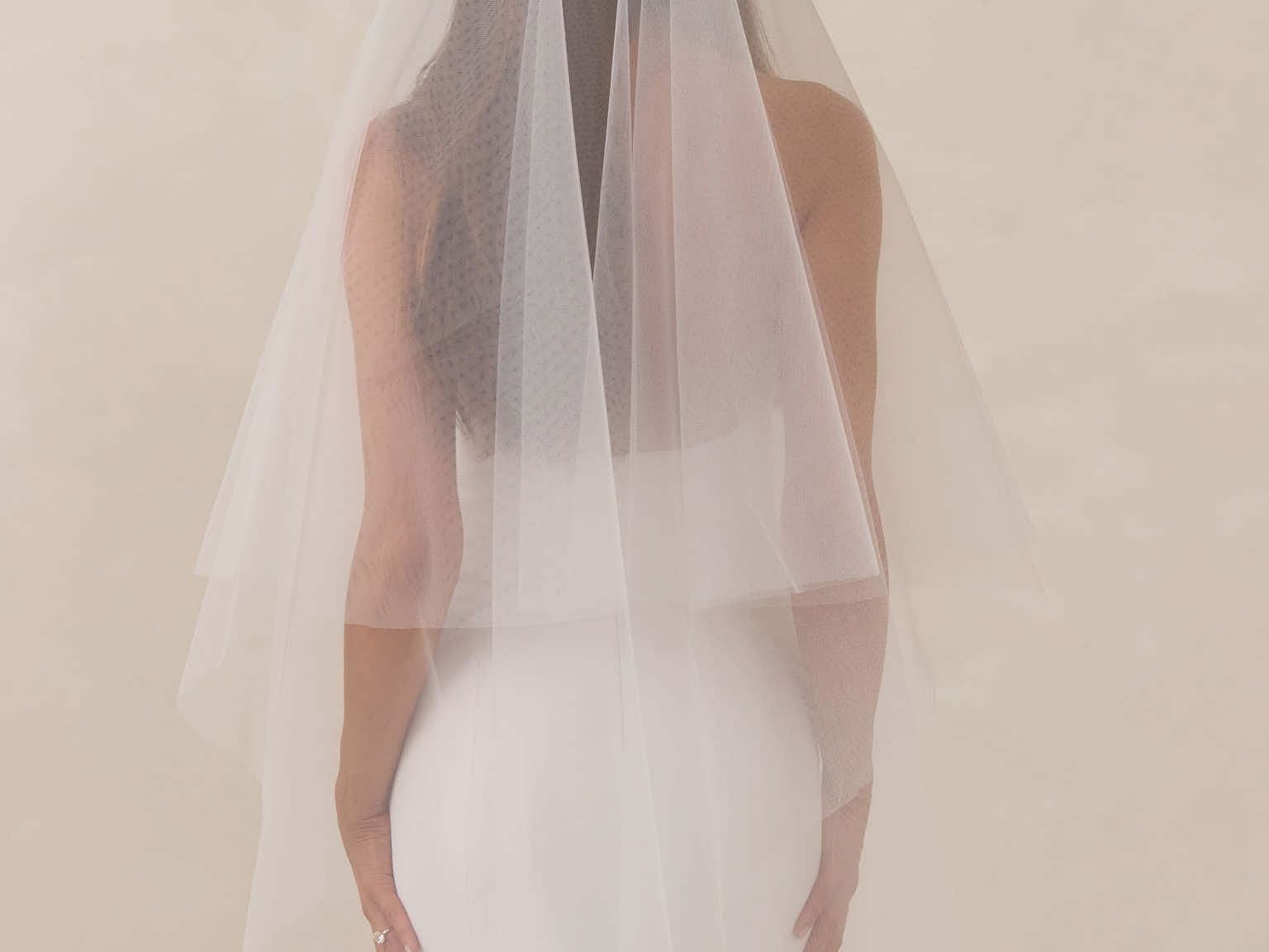 Bride wearing a white wedding dress with a fingertip length veil against a plain background