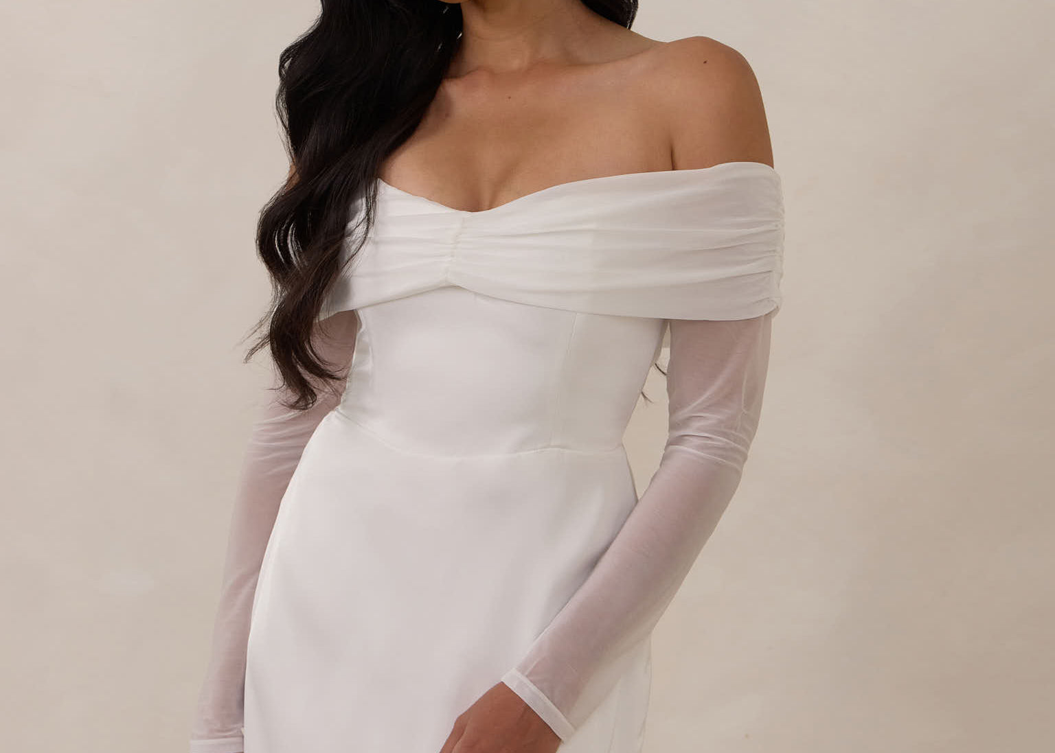 Woman wearing a white off-shoulder dress with long sleeves against a plain background