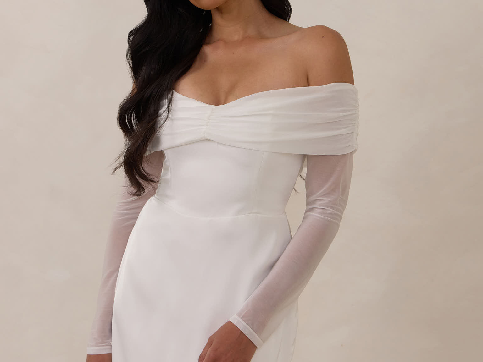 Woman wearing a white off-shoulder dress with long sleeves against a plain background