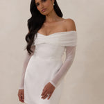 Woman wearing a white off-shoulder dress with long sleeves against a plain background