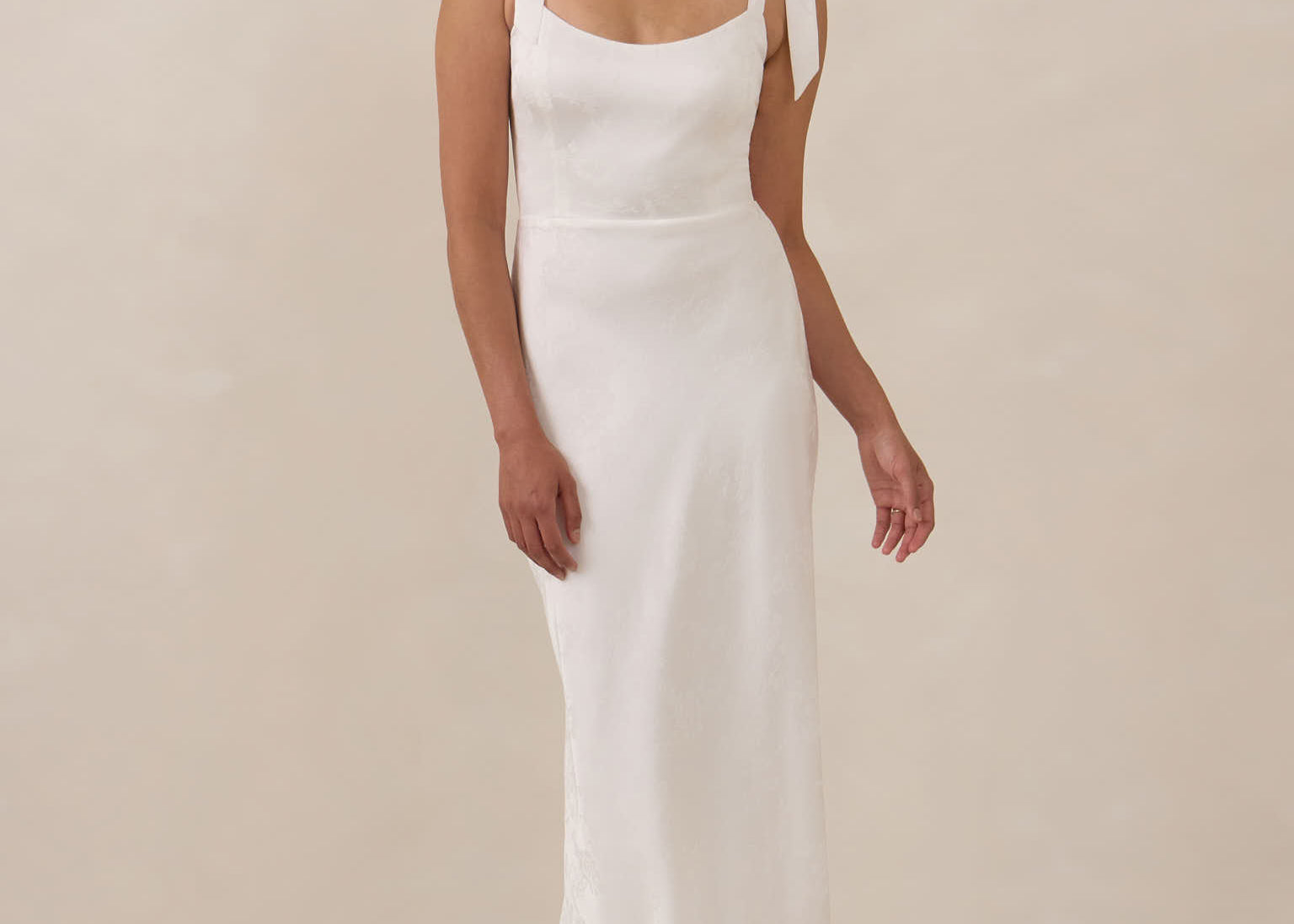 Woman wearing a white sleeveless dress against a beige background