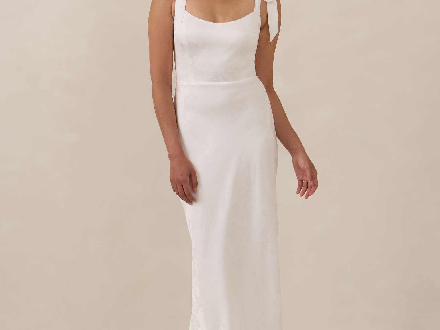 Woman wearing a white sleeveless dress against a beige background