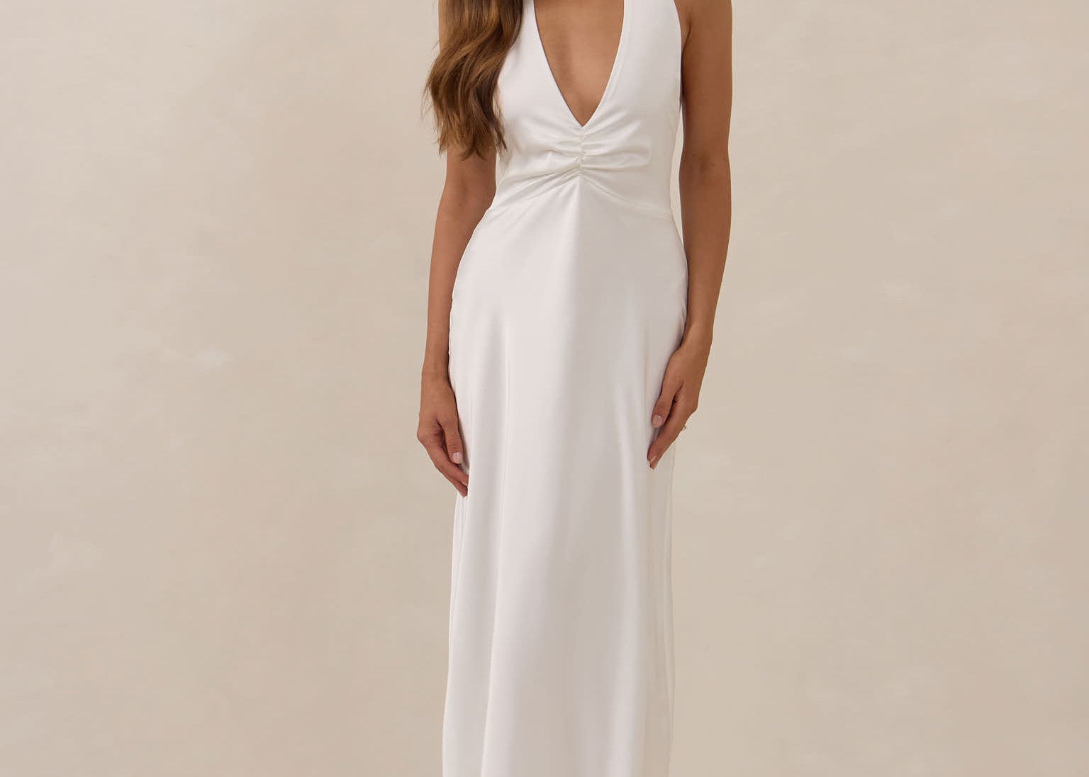 Woman wearing a white halter neck gown against a beige background