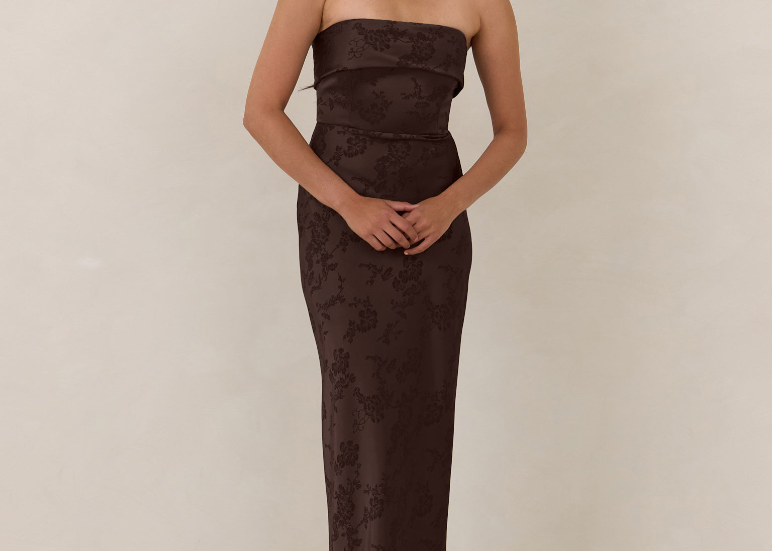 Woman wearing a strapless brown evening gown against a plain background