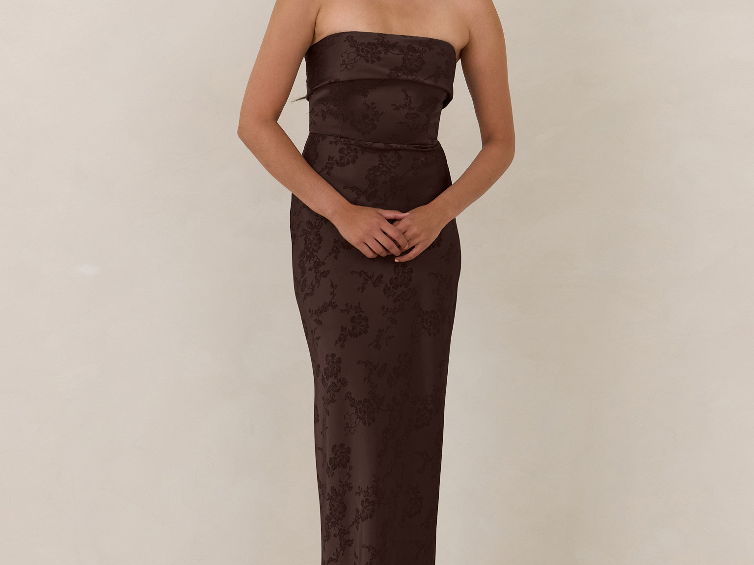 Woman wearing a strapless brown evening gown against a plain background