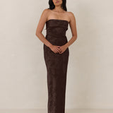 Woman wearing a strapless brown evening gown against a plain background