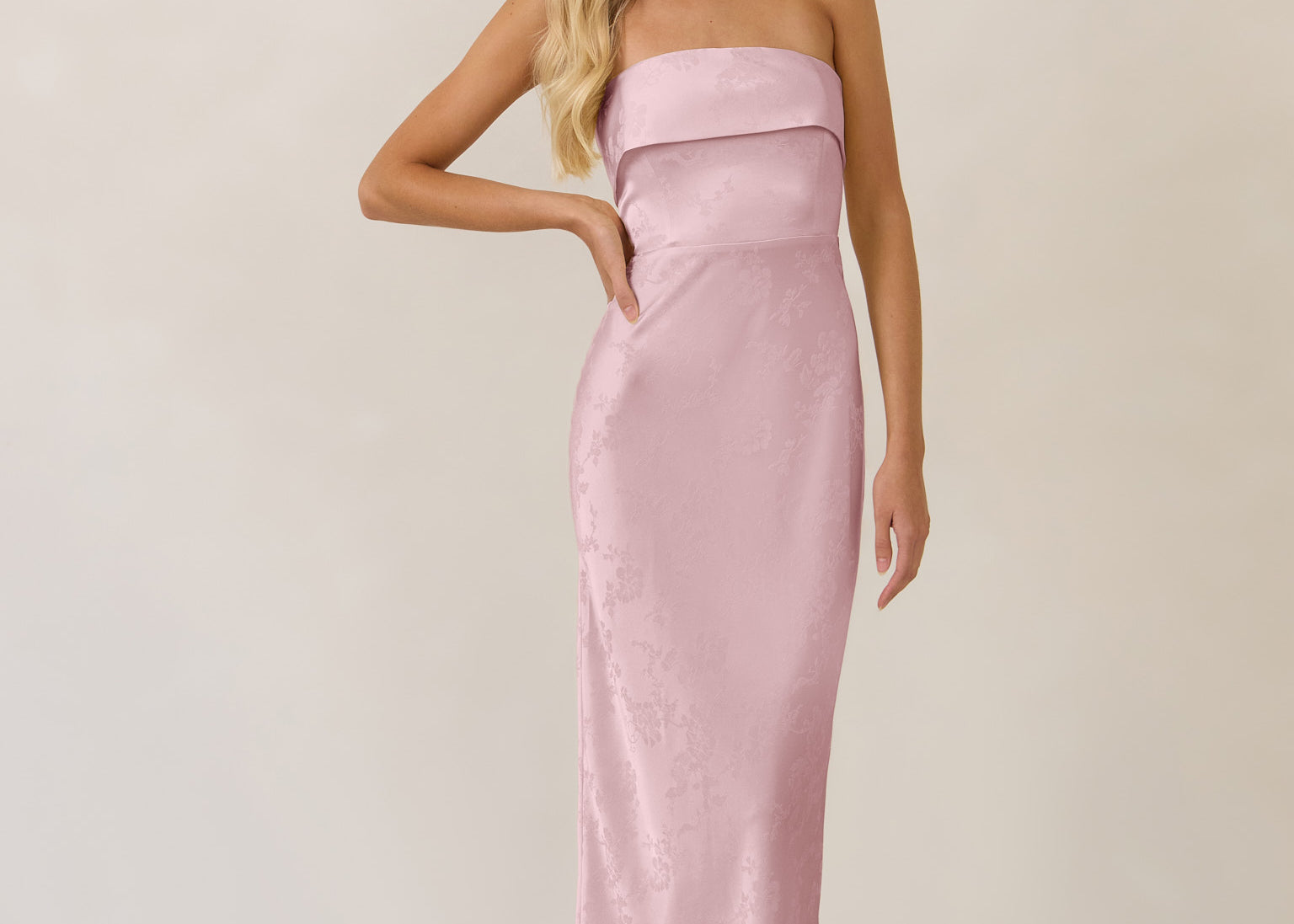 Woman wearing a strapless pink evening gown against a plain background