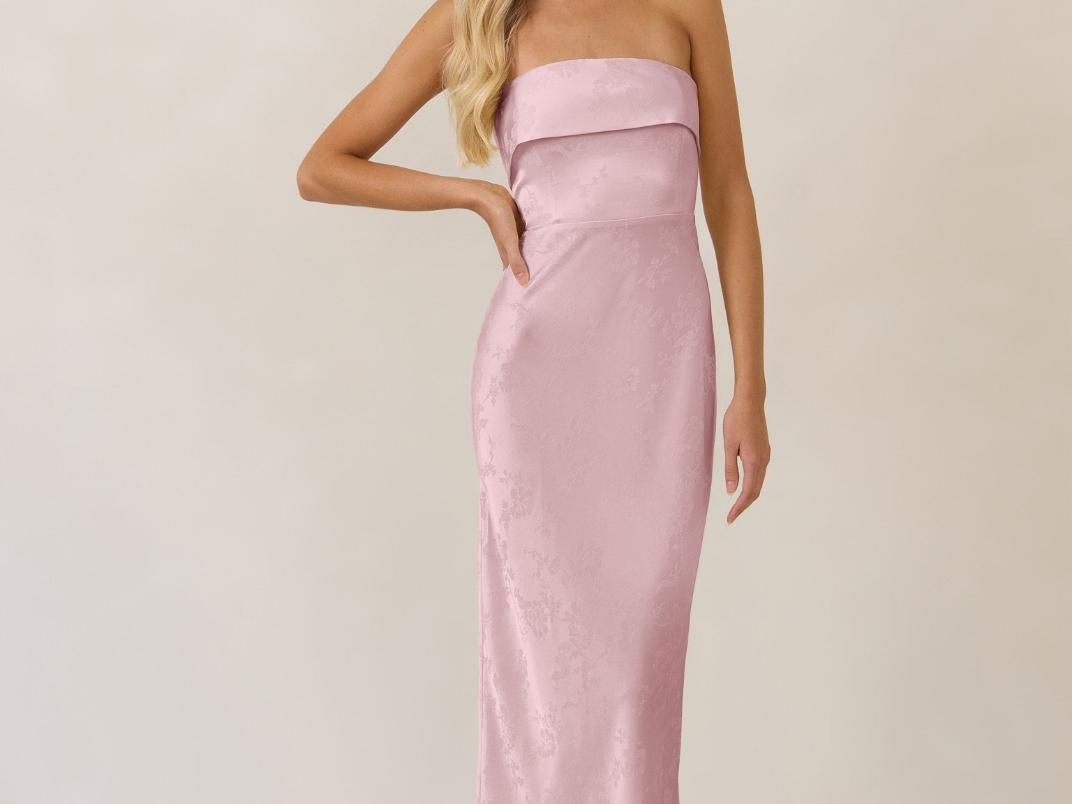 Woman wearing a strapless pink evening gown against a plain background