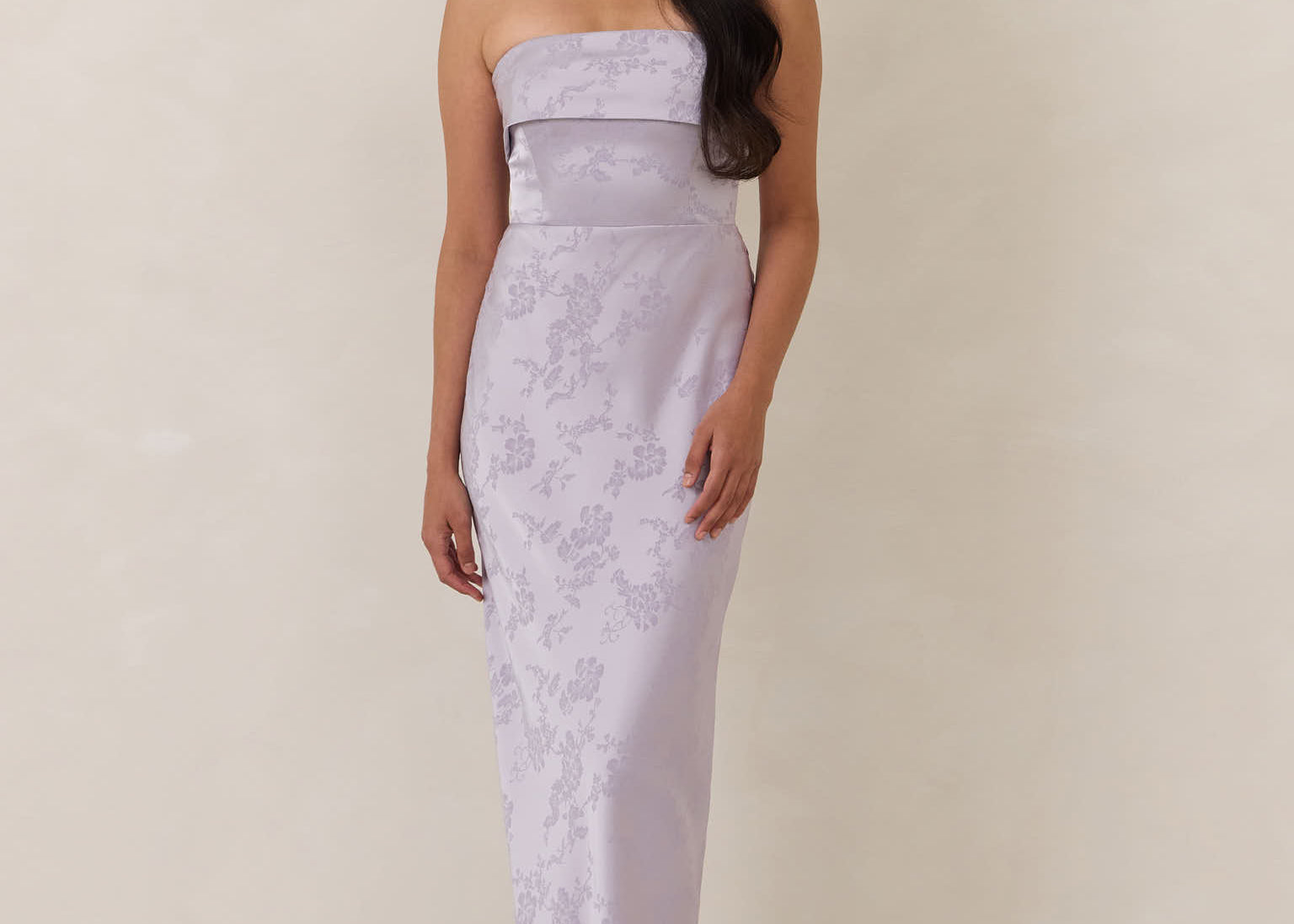 Woman wearing a strapless, lilac colored  gown against a plain background