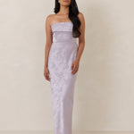 Woman wearing a strapless, lilac colored  gown against a plain background