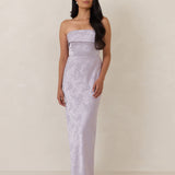 Woman wearing a strapless, lilac colored  gown against a plain background