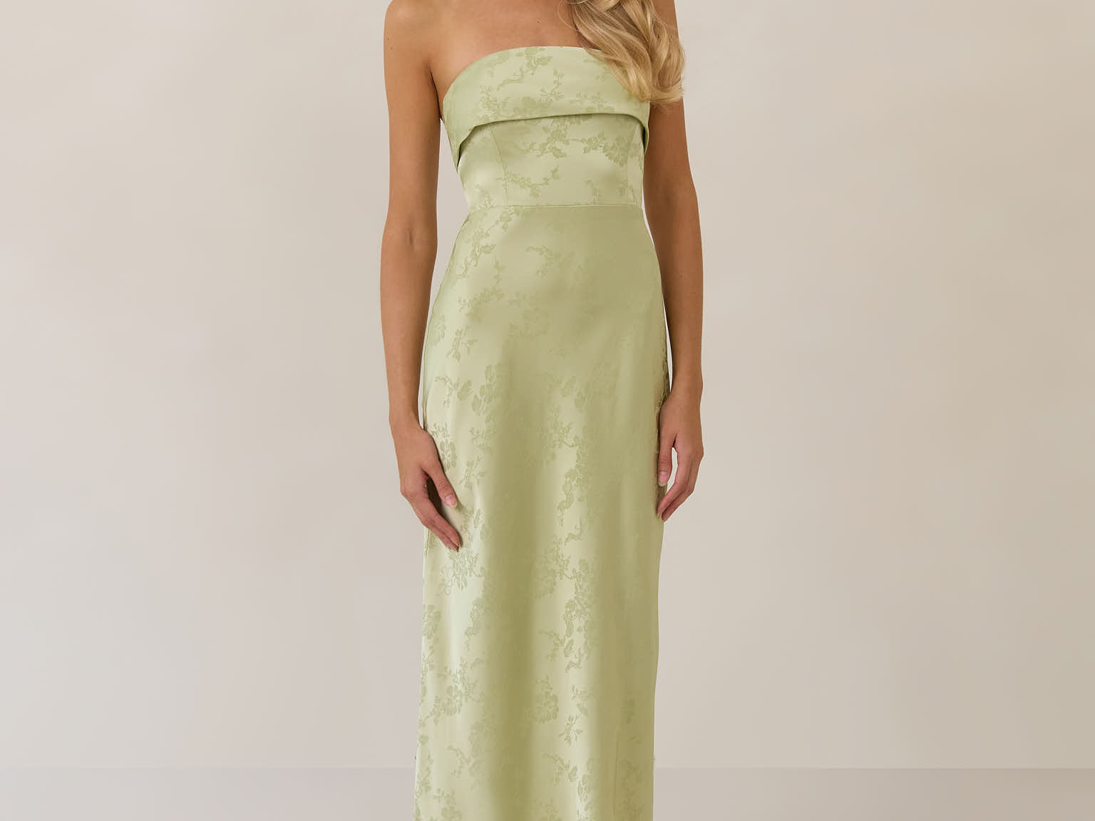 Woman wearing a strapless pistachio dress against a plain background