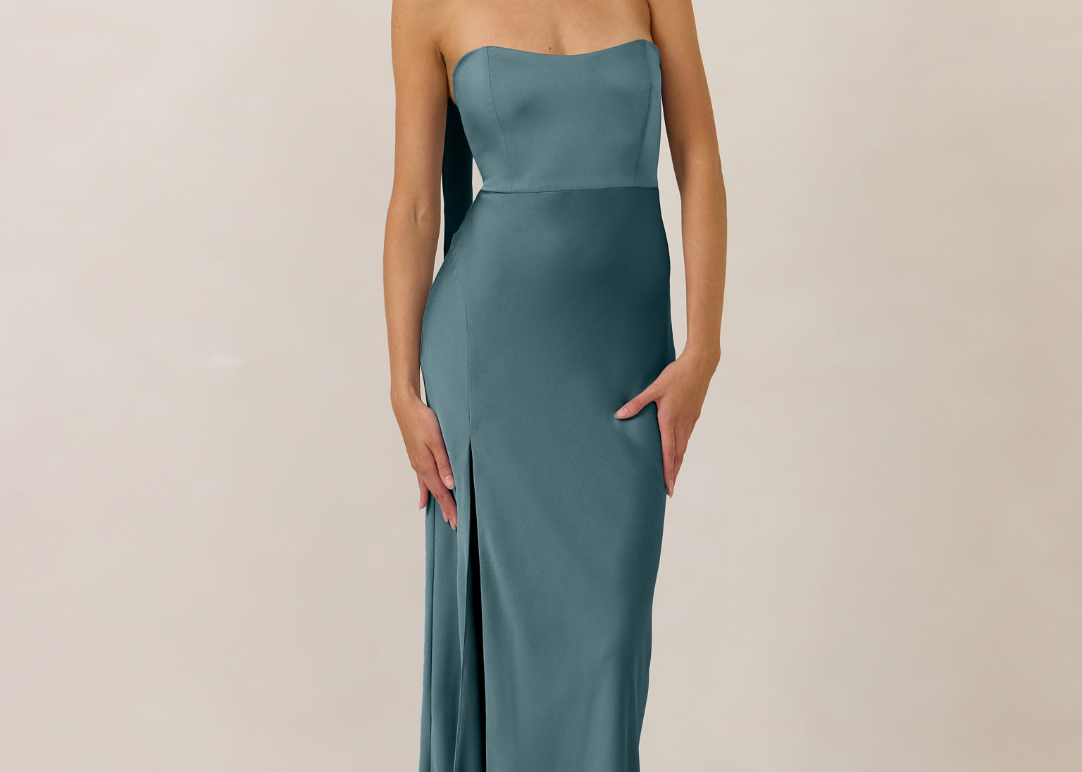 Woman wearing a strapless teal gown with a slit and neck scarf on a plain background