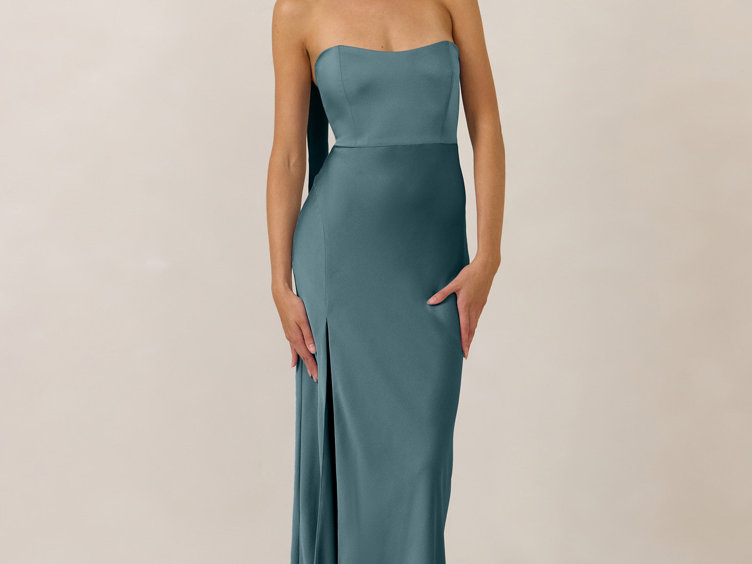 Woman wearing a strapless teal gown with a slit and neck scarf on a plain background