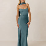 Woman wearing a strapless teal gown with a slit and neck scarf on a plain background