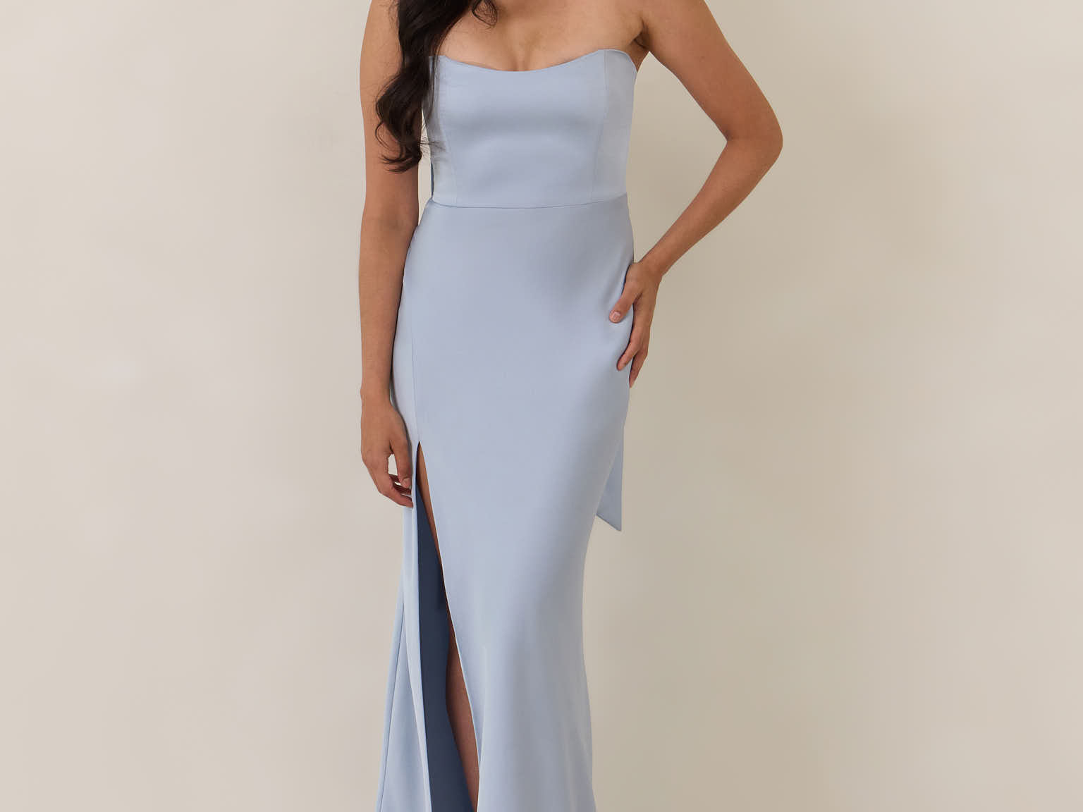 Woman wearing a light blue strapless gown with a slit on a beige background