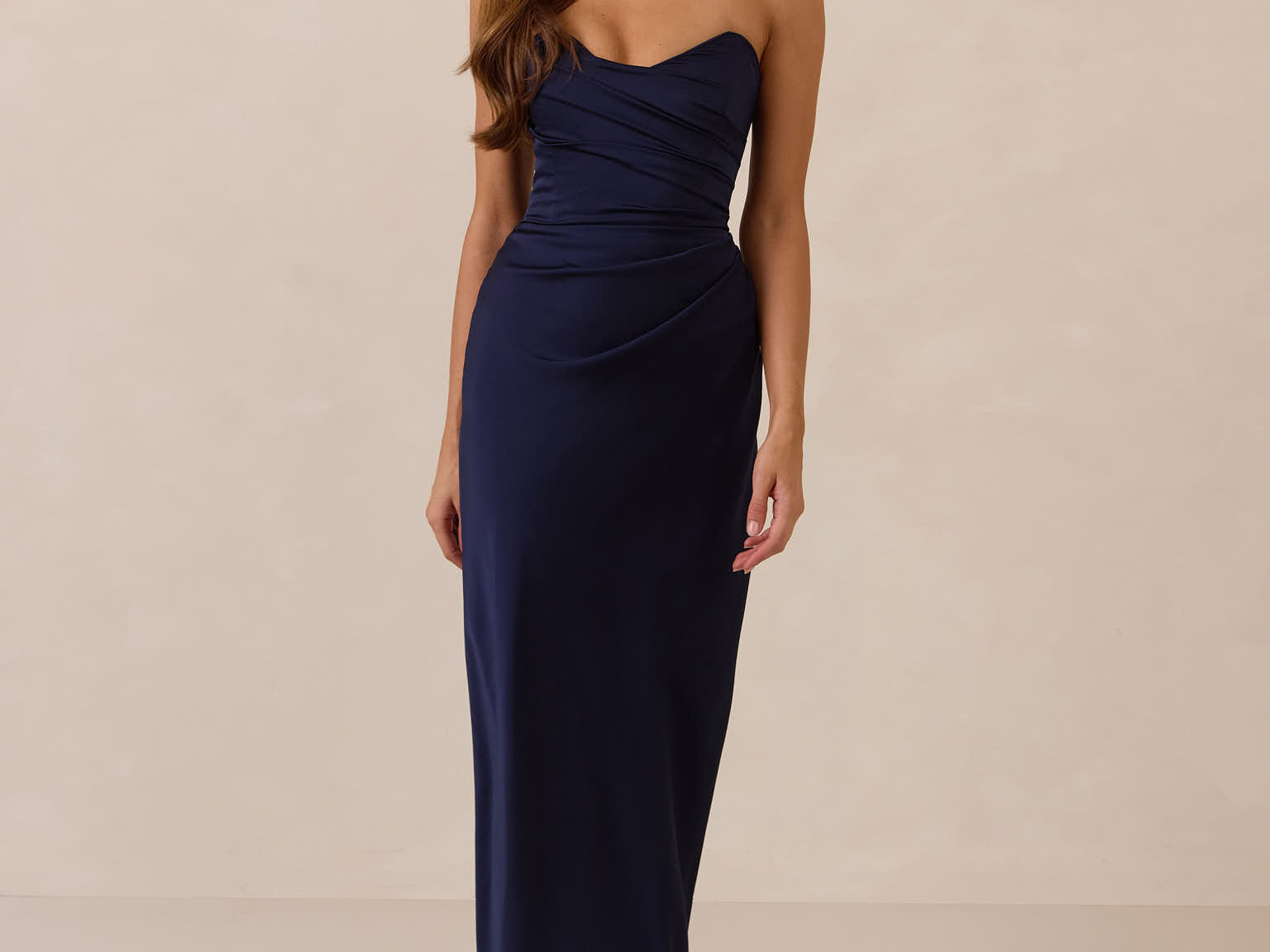 Woman wearing a navy strapless mid length dress standing against a beige background