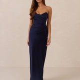 Woman wearing a navy strapless mid length dress standing against a beige background