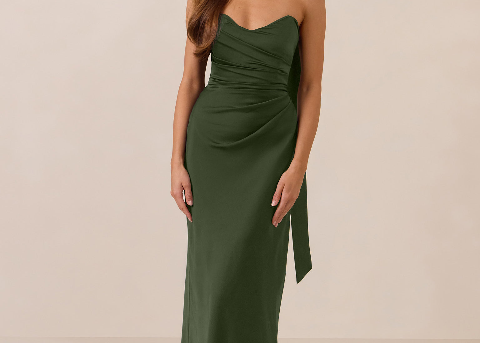 Woman wearing a green strapless dress and neck scarf standing against a beige background