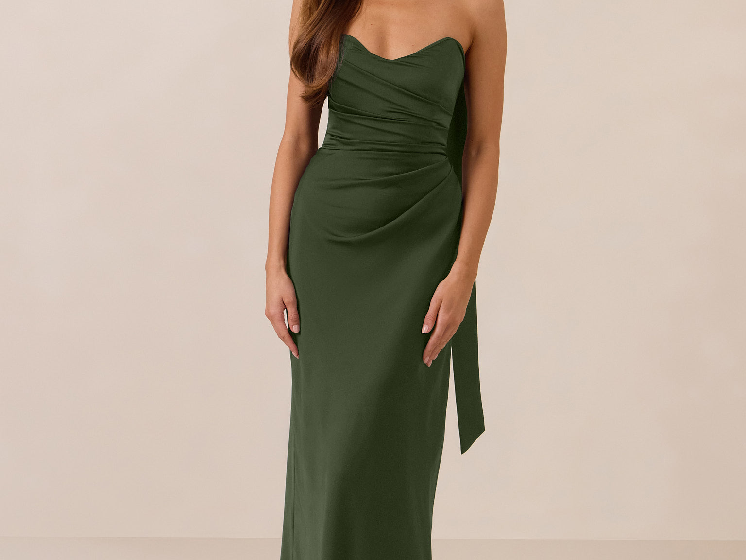 Woman wearing a green strapless dress and neck scarf standing against a beige background