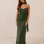 Woman wearing a green strapless dress and neck scarf standing against a beige background