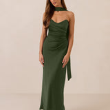 Woman wearing a green strapless dress and neck scarf standing against a beige background