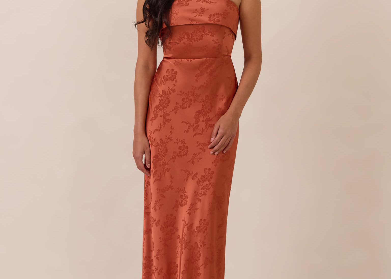 Woman wearing a clay-colored strapless gown against a beige background