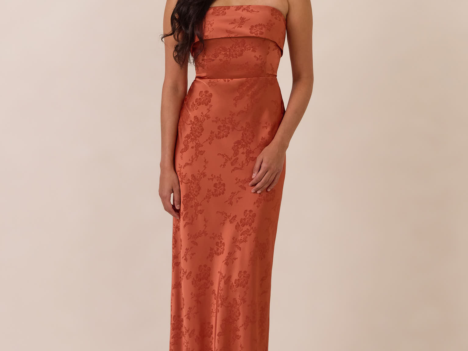 Woman wearing a clay-colored strapless gown against a beige background