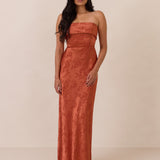 Woman wearing a clay-colored strapless gown against a beige background