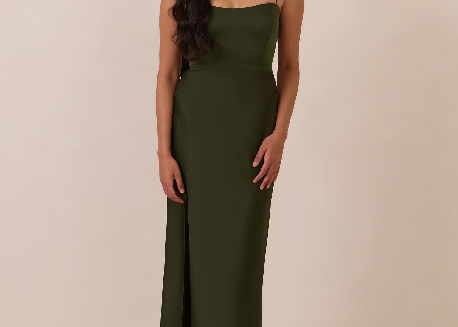 Woman wearing a dark olive coloured evening gown against a beige background
