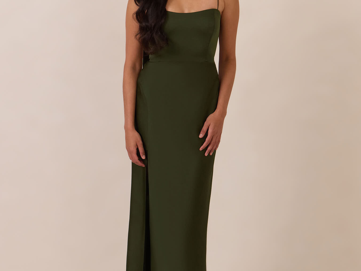 Woman wearing a dark olive coloured evening gown against a beige background