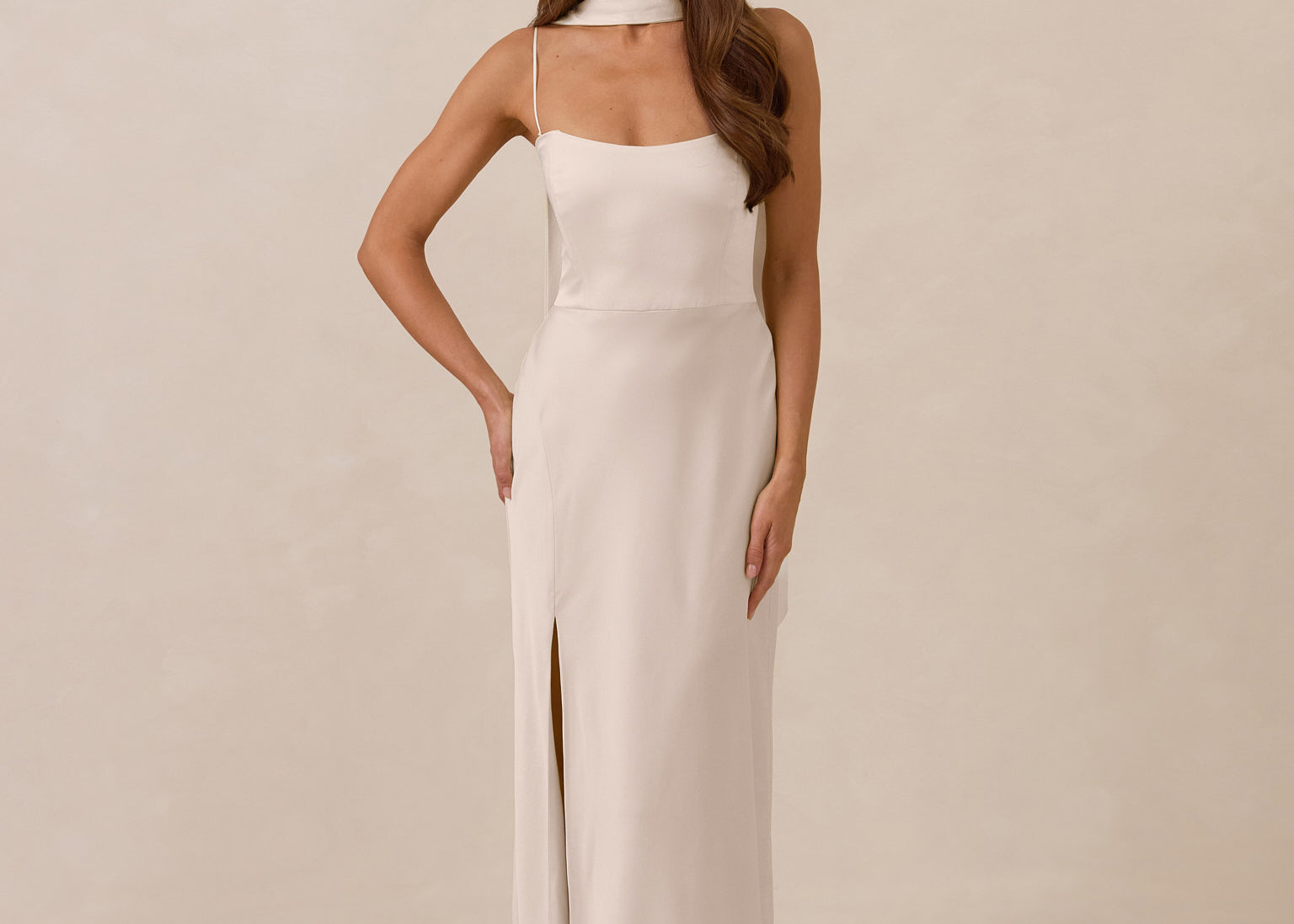 Woman wearing a long, ivory colored dress with a high slit on a beige background