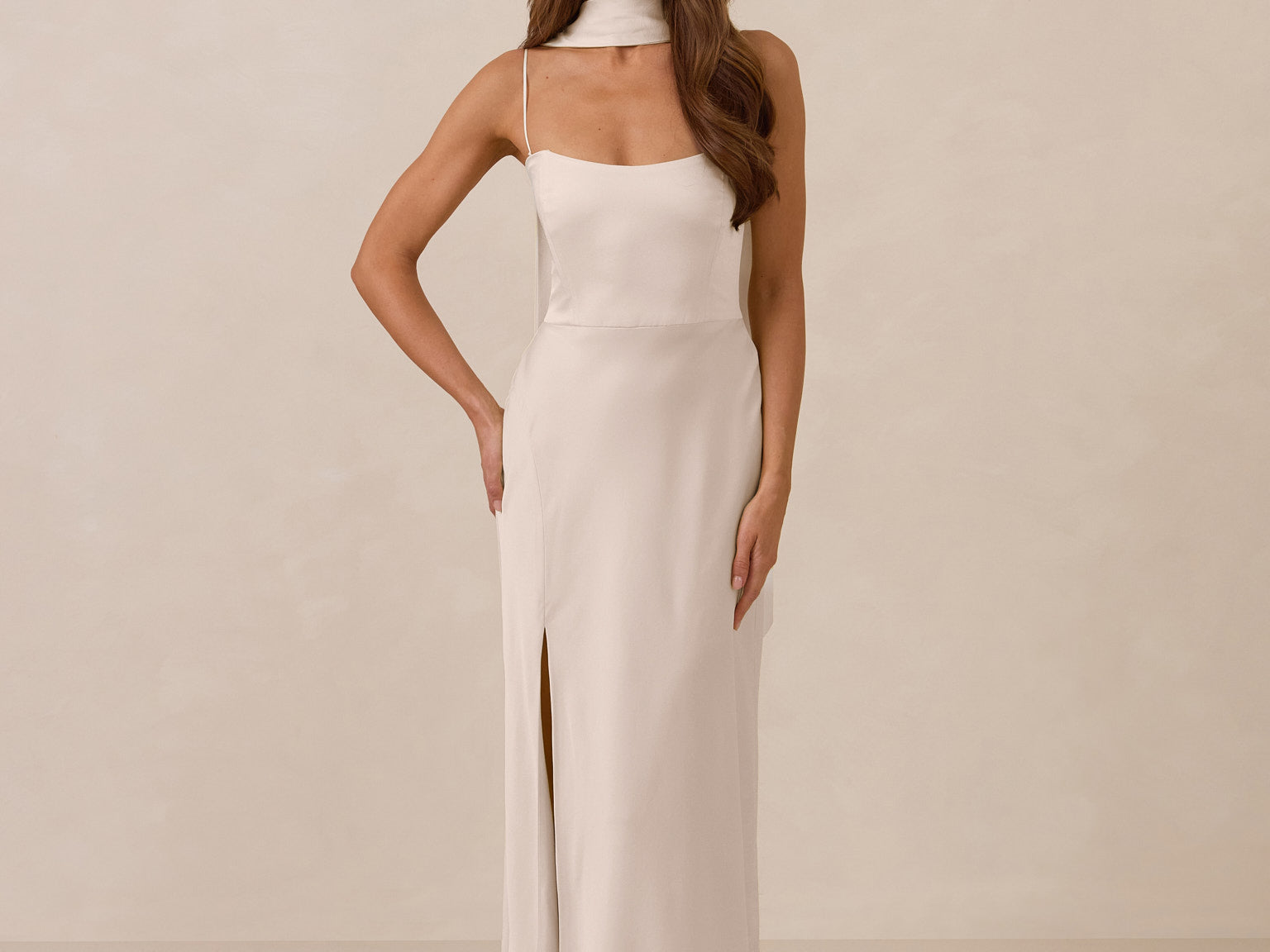 Woman wearing a long, ivory colored dress with a high slit on a beige background
