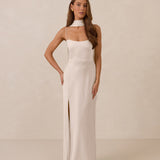 Woman wearing a long, ivory colored dress with a high slit on a beige background