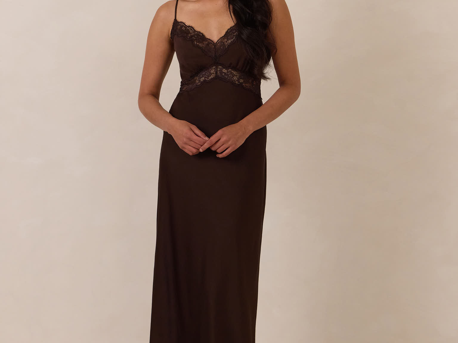 Woman wearing a brown evening gown with lace detailing standing against a plain background