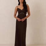 Woman wearing a brown evening gown with lace detailing standing against a plain background