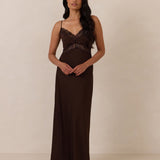 Woman wearing a brown evening gown with lace detailing standing against a plain background
