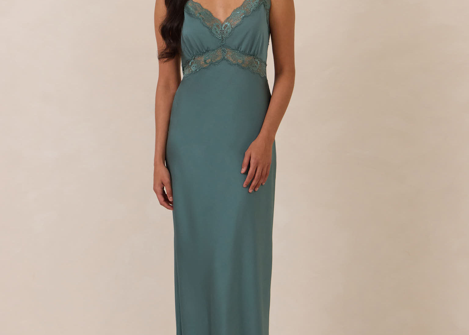 Woman wearing a teal evening gown with lace detailing on a beige background