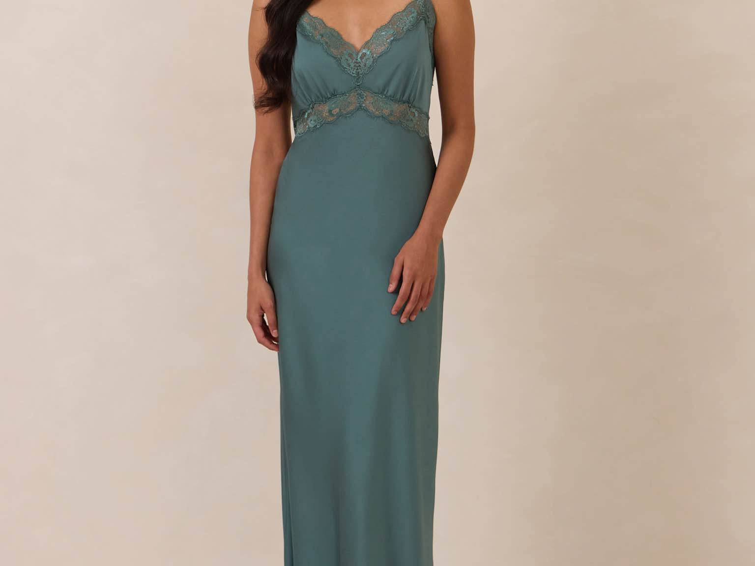 Woman wearing a teal evening gown with lace detailing on a beige background