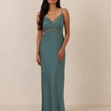 Woman wearing a teal evening gown with lace detailing on a beige background