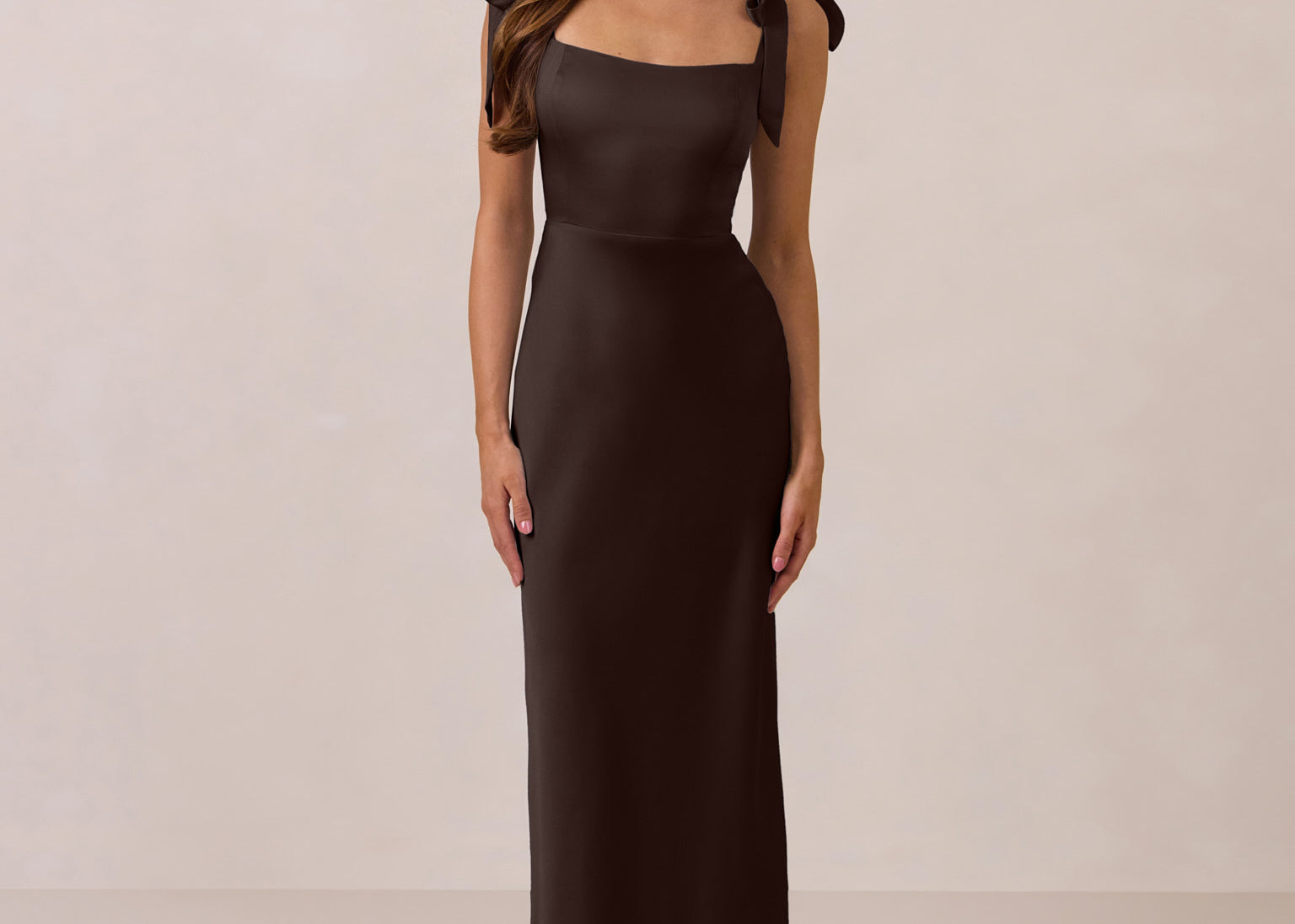 Woman wearing a dark brown evening gown with bow straps on a beige background