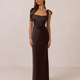 Woman wearing a dark brown evening gown with bow straps on a beige background