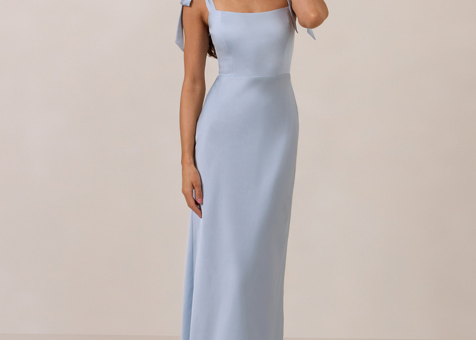 Woman wearing a light blue gown with tie straps on a beige background